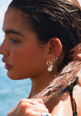[Color: Gold} Close-up of a person with earrings by the ocean