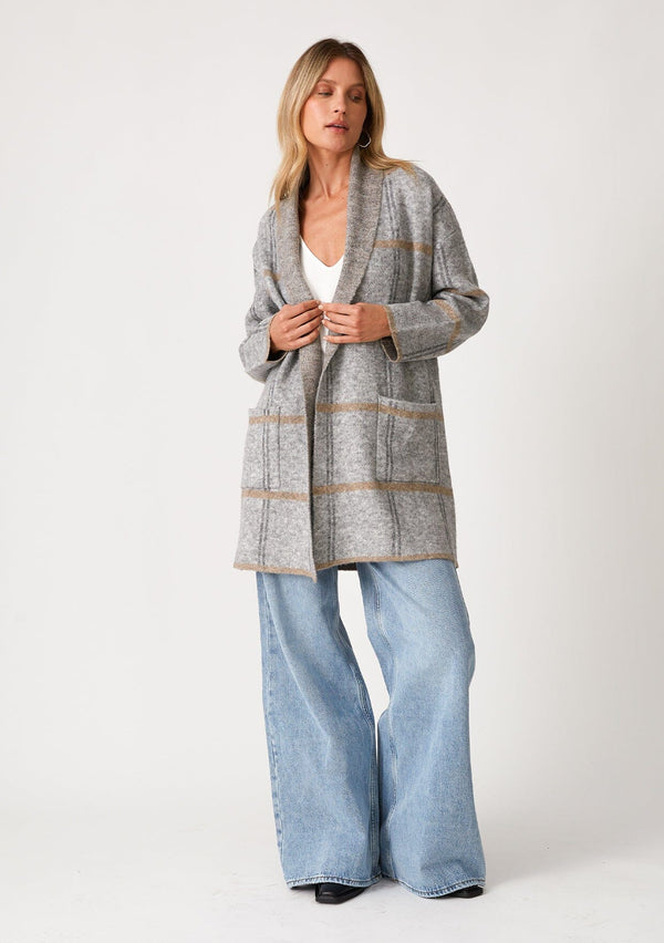 [Color: Grey/Taupe] A full body front facing image of a blonde model wearing a cozy fall cardigan in a grey windowpane plaid. With long sleeves, an open front, a shawl collar, and side pockets. 
