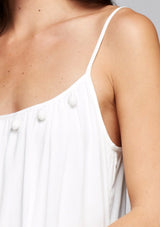 [Color: Off White] A detail image of a brunette model wearing a white maxi dress with a relaxed fit, scoop neckline with crochet ball trim, and adjustable spaghetti straps. 