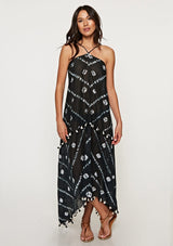 [Color: Black/Bone] A front facing image of a brunette model wearing a white and black beach maxi dress with a halter neckline, strappy open back, and a flowy silhouette with tassel trim.