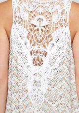 [Color: Aqua/Peach] A detail image of a brunette model wearing a sleeveless maxi dress with a an abstract print, a white chevron pattern and a crochet back panel.