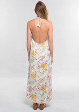 [Color: Strawberry/Gold] A back facing image of a brunette model wearing a pink and yellow floral sleeveless halter maxi dress with a relaxed, flowy silhouette and tassel ties. Styled with brown strappy sandals. 