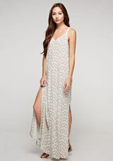 [Color: Aqua/Peach] A side facing image of a brunette model wearing a sleeveless maxi dress with an abstract print, a white chevron pattern, side slits, and a crochet back panel.