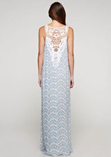 [Color: Blue/Sky] A back facing image of a brunette model wearing a sleeveless maxi dress with an abstract print, a white chevron pattern, side slits, and a crochet back panel.