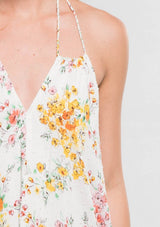 [Color: Strawberry/Gold] A detail image of a brunette model wearing a pink and yellow floral sleeveless halter maxi dress with a relaxed, flowy silhouette and tassel ties. Styled with brown strappy sandals. 