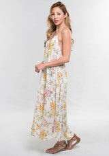 [Color: Strawberry/Gold] A side facing image of a brunette model wearing a pink and yellow floral sleeveless halter maxi dress with a relaxed, flowy silhouette and tassel ties. Styled with brown strappy sandals. 