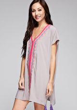 [Color: Grey] A side facing image of a brunette model wearing a grey and pink embroidered tunic with a tassel accent at the hem.