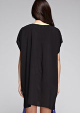 [Color: Black] A back facing image of a brunette model wearing a black embroidered tunic with embroidery and a tassel accent at the hem.