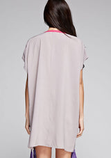 [Color: Grey] A back facing image of a brunette model wearing a grey and pink embroidered tunic with a tassel accent at the hem.