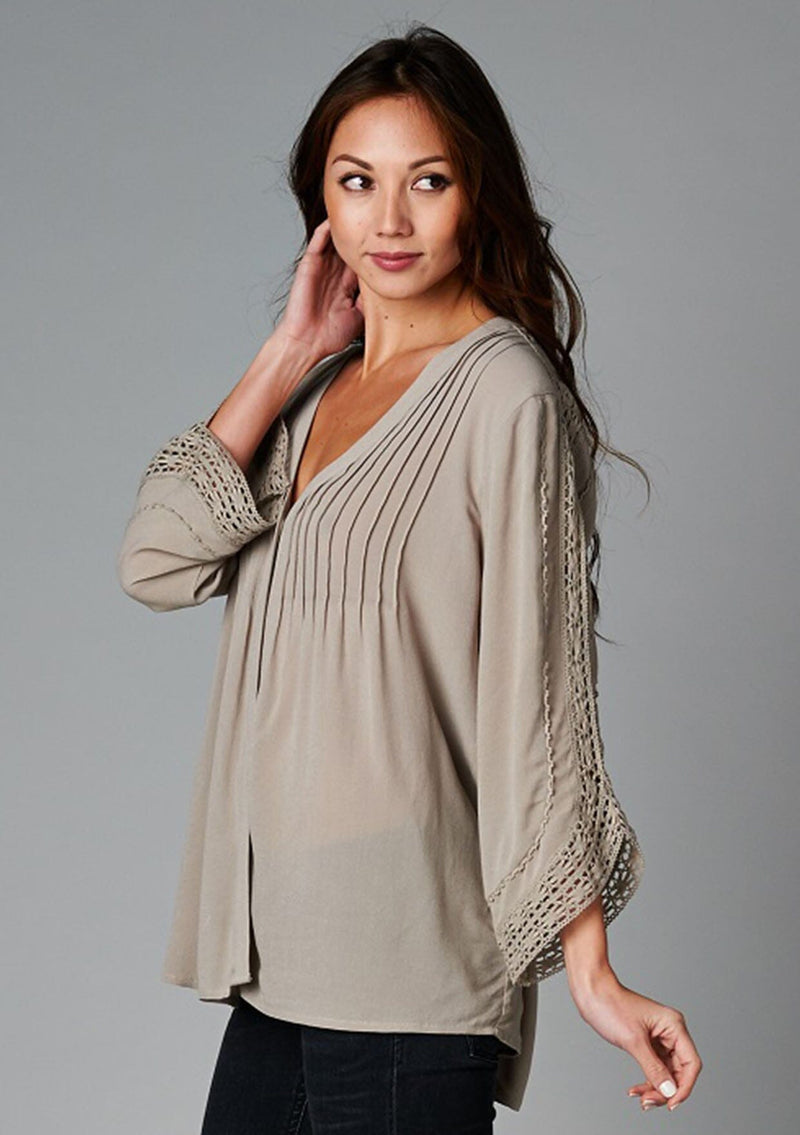 [Color: Taupe] A side facing image of a brunette model wearing a bohemian v-neck blouse with lace crochet detail at the sleeve.