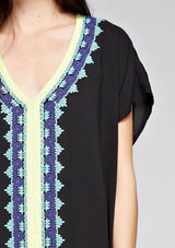 [Color: Black] A detail image of a brunette model wearing a black embroidered tunic with embroidery and a tassel accent at the hem.