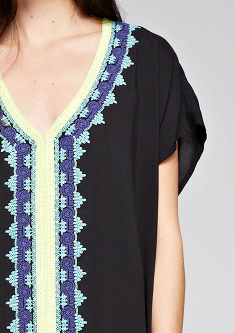 [Color: Black] A detail image of a brunette model wearing a black embroidered tunic with embroidery and a tassel accent at the hem.