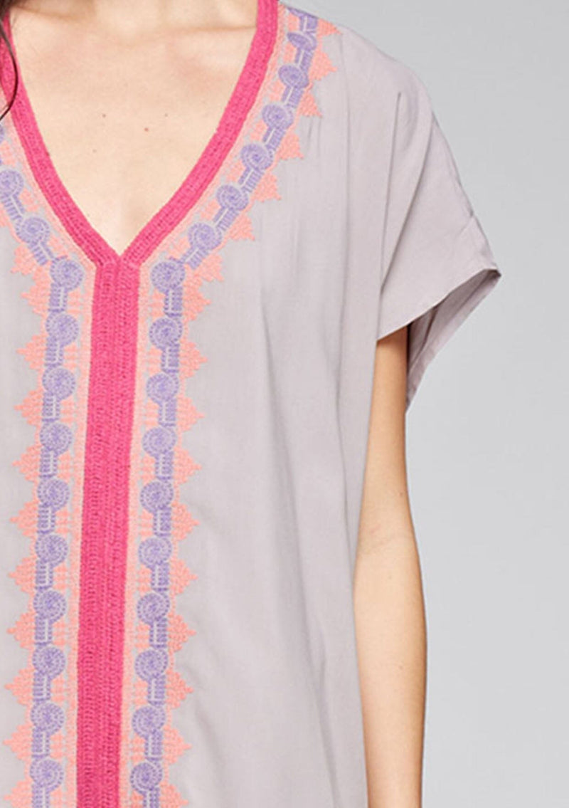[Color: Grey] A detail image of a brunette model wearing a grey and pink embroidered tunic with a tassel accent at the hem.