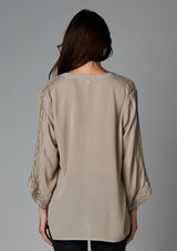 [Color: Taupe] A back facing image of a brunette model wearing a bohemian v-neck blouse with lace crochet detail at the sleeve.