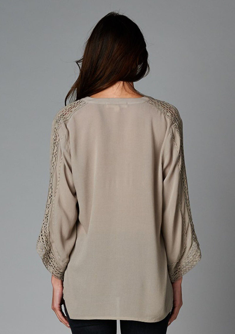 [Color: Taupe] A back facing image of a brunette model wearing a bohemian v-neck blouse with lace crochet detail at the sleeve.