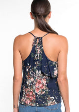 [Color: Navy/Blush/Olive] A back facing image of a brunette model wearing a navy blue floral tank top with a flowy ruffle front and tie back detail. 