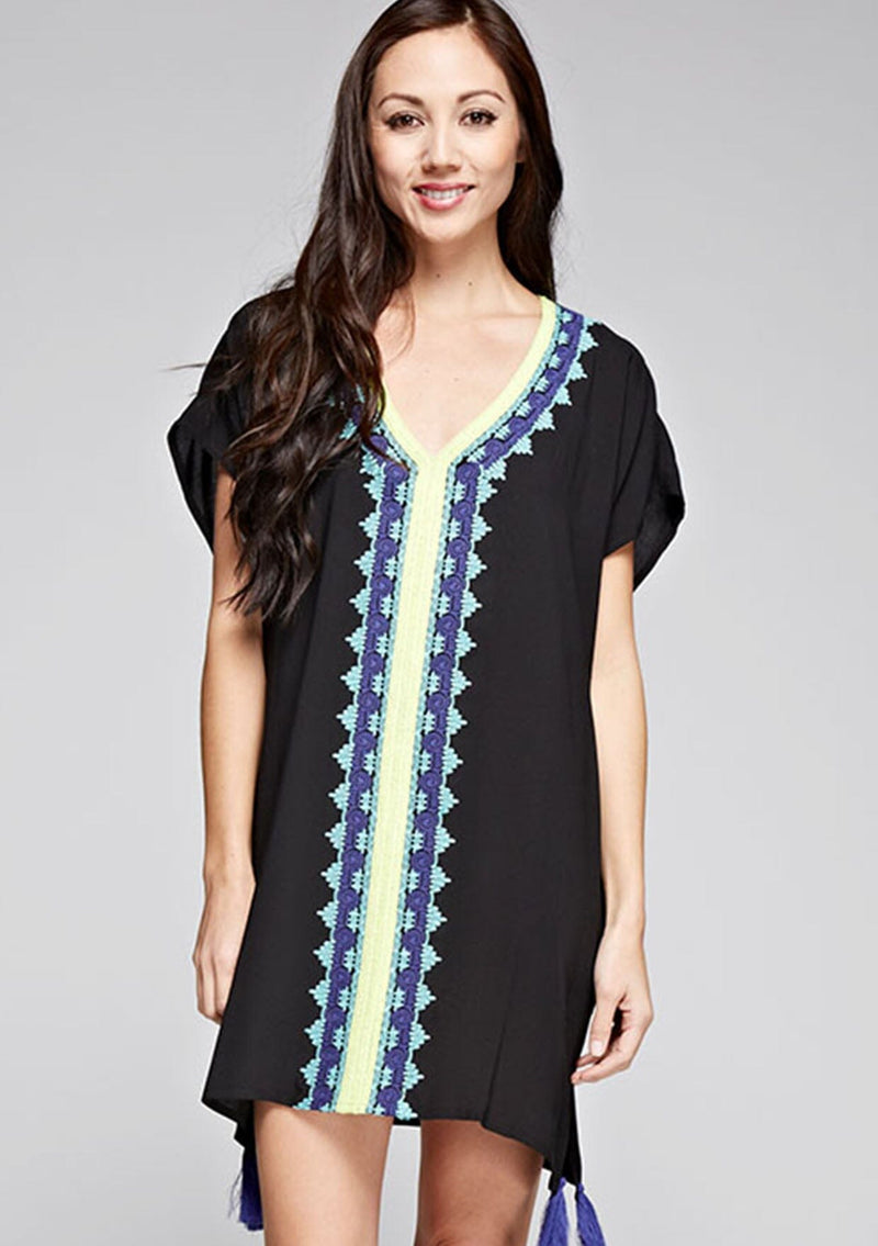 [Color: Black] A front facing image of a brunette model wearing a black embroidered tunic with embroidery and a tassel accent at the hem.