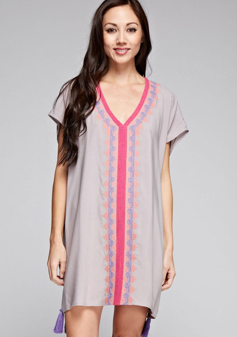 [Color: Grey] A front facing image of a brunette model wearing a grey and pink embroidered tunic with a tassel accent at the hem.
