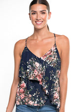 [Color: Navy/Blush/Olive] A front facing image of a brunette model wearing a navy blue floral tank top with a flowy ruffle front and tie back detail. 