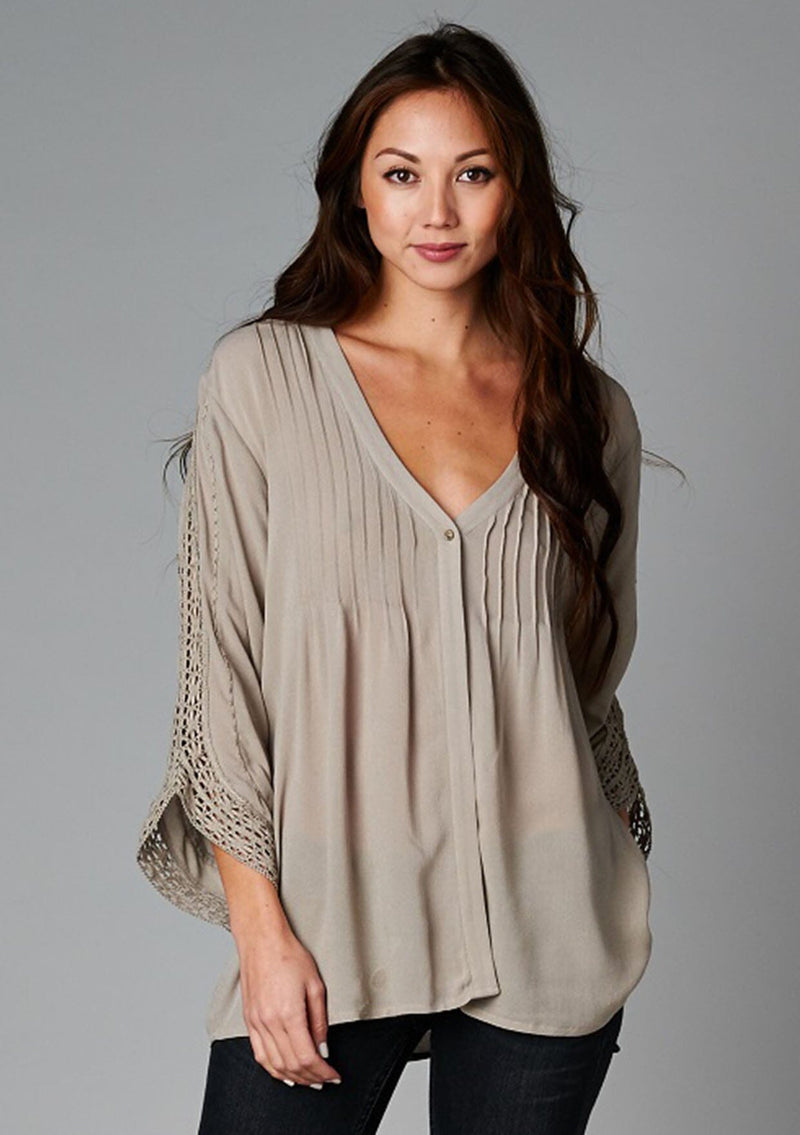 [Color: Taupe] A front facing image of a brunette model wearing a bohemian v-neck blouse with lace crochet detail at the sleeve.