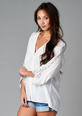 [Color: Off White] A front facing image of a brunette model wearing a bohemian white v-neck blouse with lace crochet detail at the sleeve.