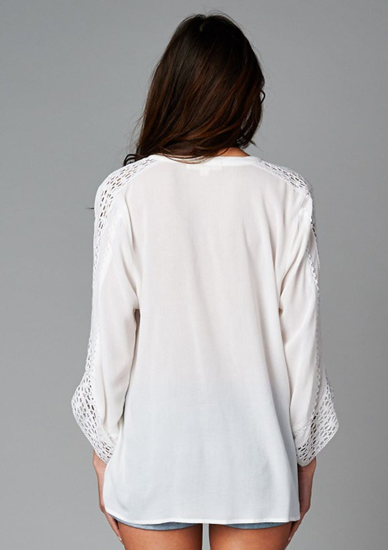 [Color: Off White] A back facing image of a brunette model wearing a bohemian white v-neck blouse with lace crochet detail at the sleeve.