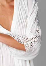 [Color: Off White] A detail image of a brunette model wearing a bohemian white v-neck blouse with lace crochet detail at the sleeve.