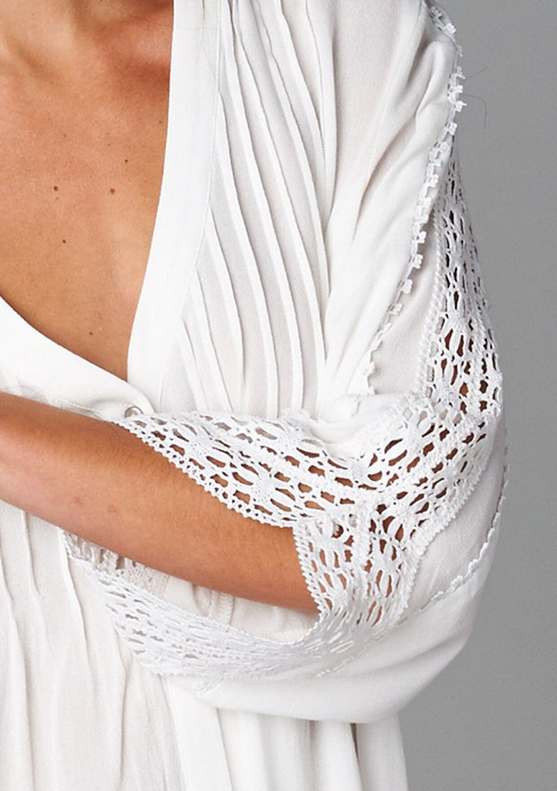 [Color: Off White] A detail image of a brunette model wearing a bohemian white v-neck blouse with lace crochet detail at the sleeve.