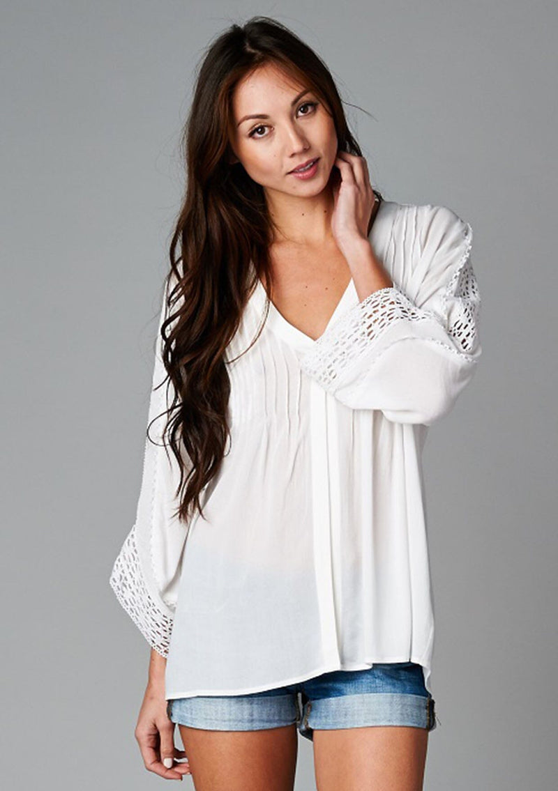 [Color: Off White] A front facing image of a brunette model wearing a bohemian white v-neck blouse with lace crochet detail at the sleeve.