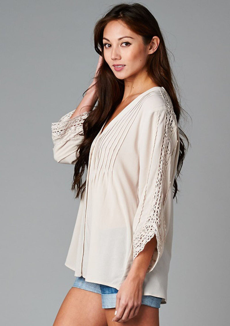 [Color: Champagne] A side facing image of a brunette model wearing a bohemian v-neck blouse with lace crochet detail at the sleeve.