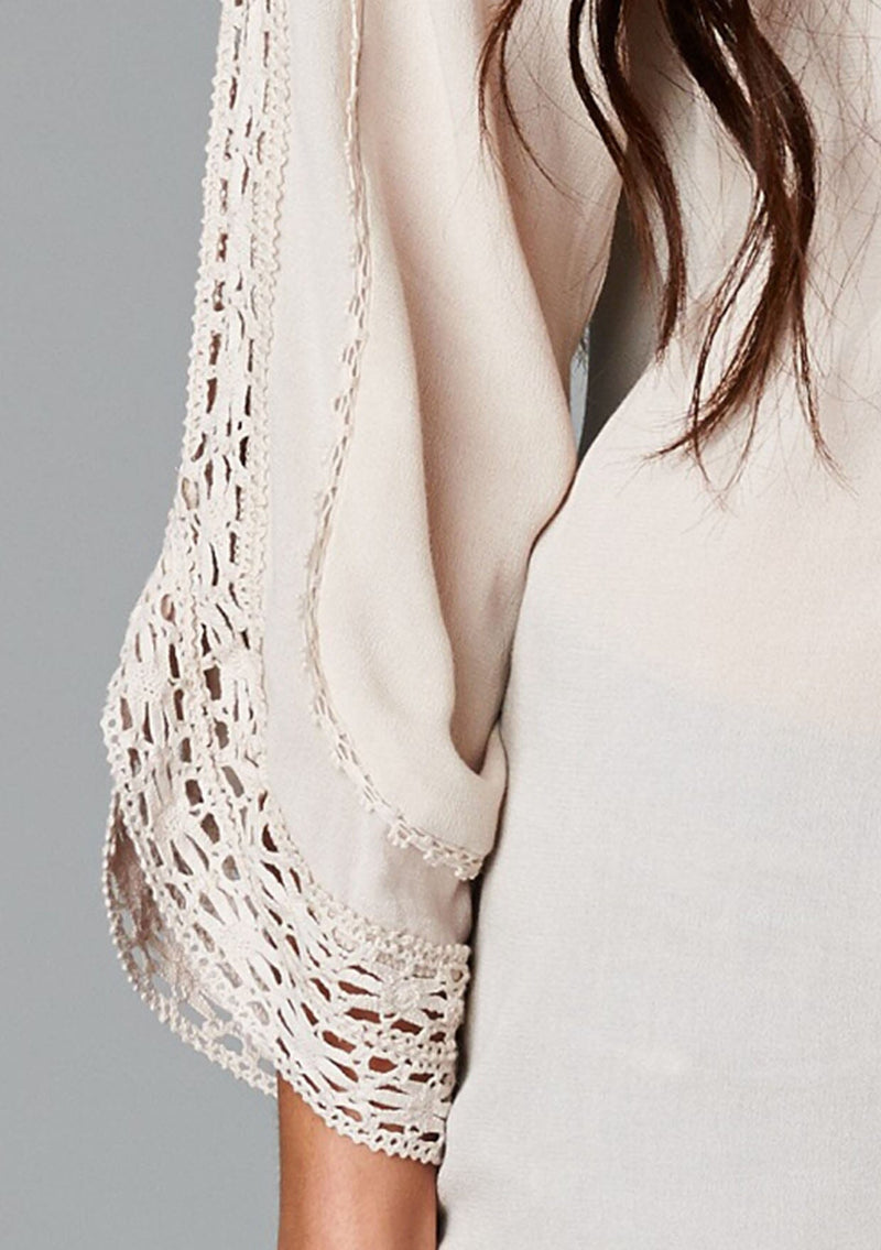 [Color: Champagne] A detail image of a brunette model wearing a bohemian v-neck blouse with lace crochet detail at the sleeve.