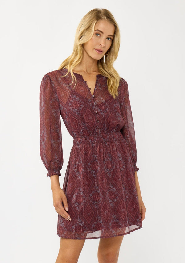 [Color: Wine/Rose] A front facing image of a blonde model wearing a floral diamond print chiffon mini dress with metallic thread details, 3/4 sleeves, a button front, and an elastic waist. A special occasion dress for weddings and holidays. 