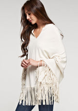 [Color: Vanilla] A side facing image of a blonde model wearing an ivory suede fringed poncho. 