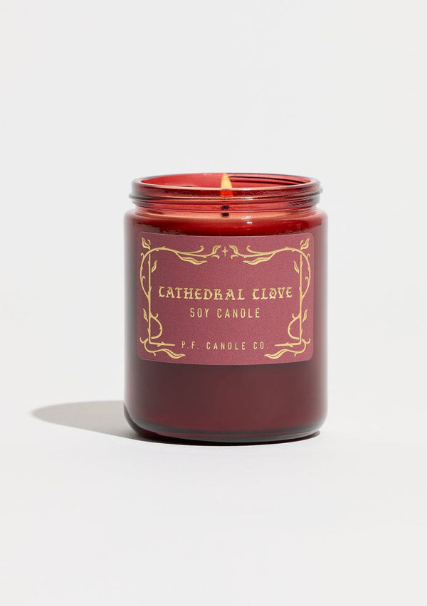 A fall and holiday candle in a burgundy glass jar labeled “P.F. Candle Co. Cathedral Clove.”