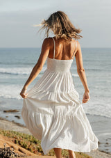 [Color: Natural/Blue] A back image of a blonde model wearing a striped maxi dress with a tiered skirt, v-neckline, adjustable spaghetti straps, smocked back, and side pockets. 