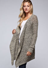 [Color: Black/Natural] A side facing image of a blonde model wearing a marled knit black and beige cardigan with a shawl collar and cozy long sleeves. A casual fall cardigan. 