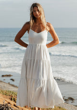 [Color: Natural/Blue] A front image of a blonde model wearing a striped maxi dress with a tiered skirt, v-neckline, adjustable spaghetti straps, smocked back, and side pockets. 