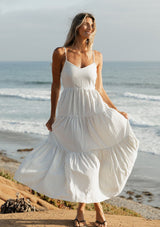 [Color: Natural/Blue] A front image of a blonde model wearing a striped maxi dress with a tiered skirt, v-neckline, adjustable spaghetti straps, smocked back, and side pockets. 