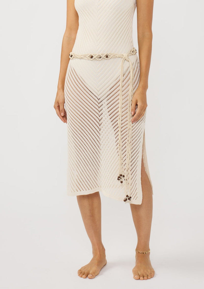 [Color: Ivory] A brunette model wearing a crochet dress with a long bohemian macrame belt with beads wrapped around the dress. 