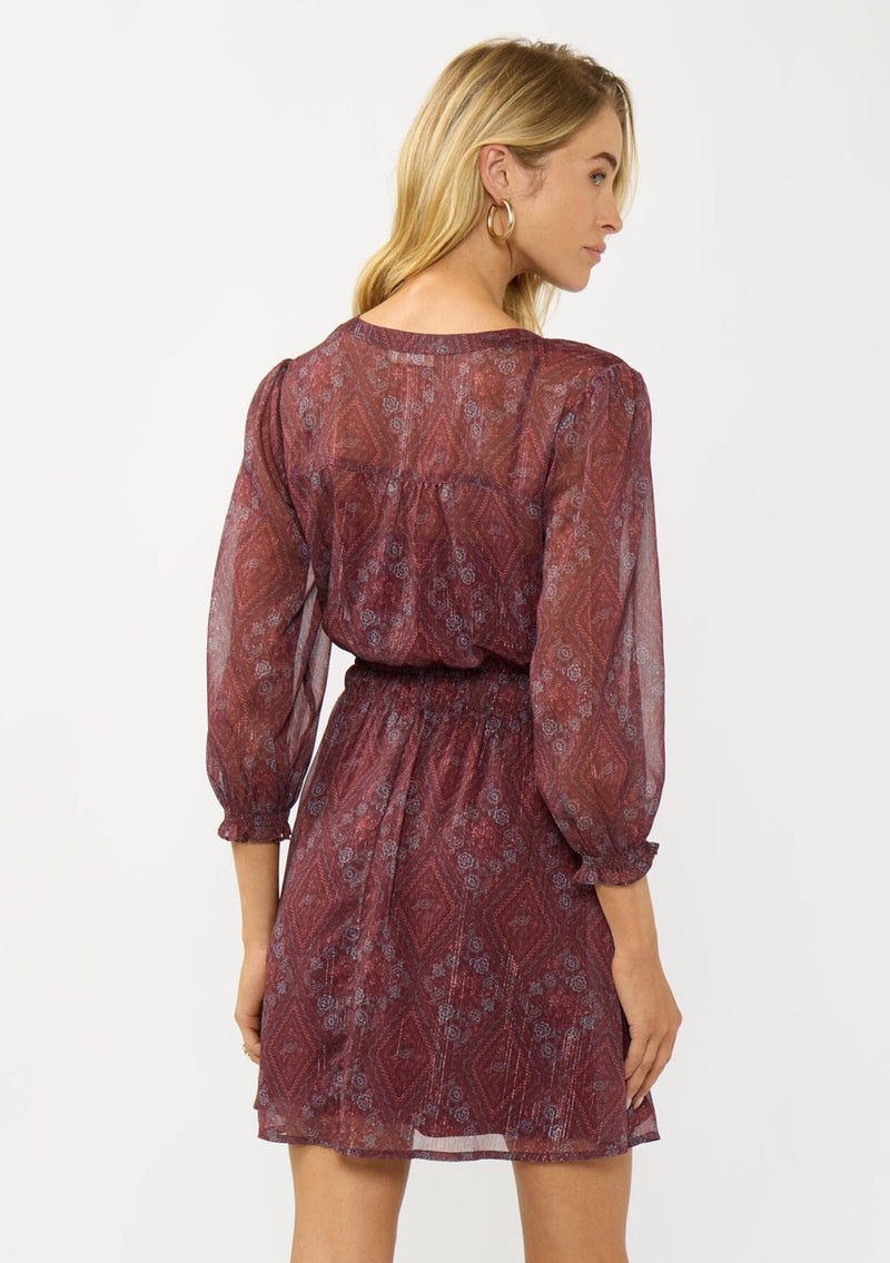 [Color: Wine/Rose] A back facing image of a blonde model wearing a floral diamond print chiffon mini dress with metallic thread details, 3/4 sleeves, a button front, and an elastic waist. A special occasion dress for weddings and holidays. 