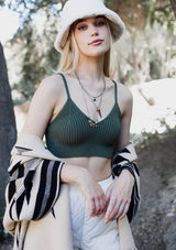 [Color: Olive] A blonde model wearing a rib knit crop top in olive green. Featuring a v neckline, spaghetti straps, and a body hugging silhouette. A soft and cozy top crafted in stretchy fabric, perfect for layering or wearing on its own. 