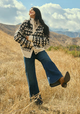 [Color: Cream/Black] A front facing image of a brunette model wearing a black and cream button front knit sweater with a high neckline and side pockets. A bohemian knit sweater for cozy fall styling. 
