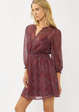 [Color: Wine/Rose] A side facing image of a blonde model wearing a floral diamond print chiffon mini dress with metallic thread details, 3/4 sleeves, a button front, and an elastic waist. A special occasion dress for weddings and holidays. 