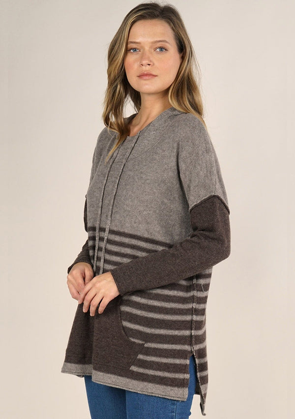 [Color: Cement/Dark Chocolate] An image of a blonde model wearing a grey and brown striped pullover hoodie with a contrast sleeve, drawstring, and kangaroo pockets. Casual and laid back for the fall season. 
