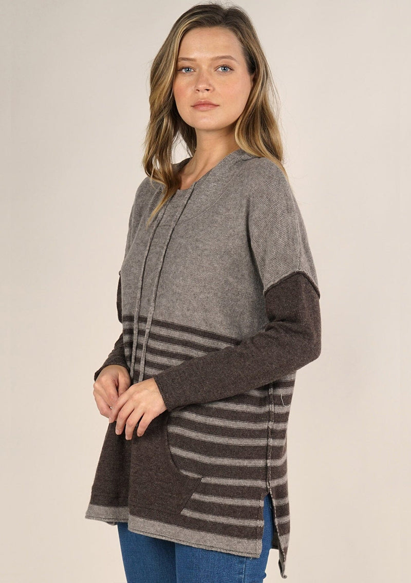 [Color: Cement/Dark Chocolate] An image of a blonde model wearing a grey and brown striped pullover hoodie with a contrast sleeve, drawstring, and kangaroo pockets. Casual and laid back for the fall season. 