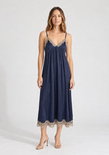 [Color: Navy/Taupe] A front facing image of a blonde model wearing a navy blue lace midi dress with spaghetti straps and an empire waist. 