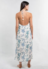 [Color: Ocean/Blue] A back facing image of a brunette model wearing a blue and white floral sleeveless halter maxi dress with a relaxed, flowy silhouette and tassel ties. Styled with brown strappy sandals. 