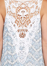 [Color: Blue/Sky] A detail image of a brunette model wearing a sleeveless maxi dress with an abstract print, a white chevron pattern, side slits, and a crochet back panel.
