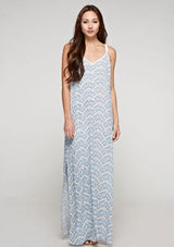 [Color: Blue/Sky] A side facing image of a brunette model wearing a sleeveless maxi dress with an abstract print, a white chevron pattern, side slits, and a crochet back panel.
