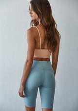 [Color: Peach] A back facing image of a brunette model wearing a basic light orange bralette cami with a slim stretchy fit and a v neckline.